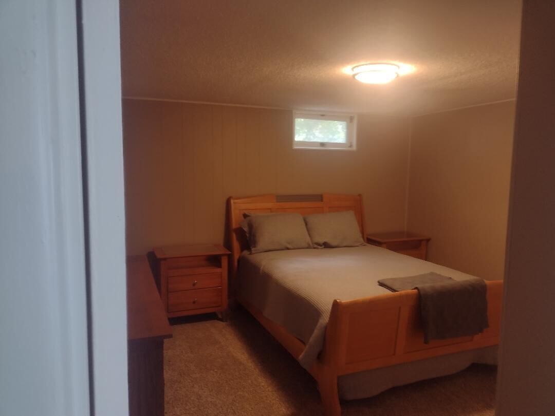 Un dormitorio con una cama individual, una mesita de noche, un aparador y un ventanal pequeño.