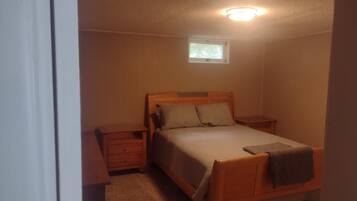 Un dormitorio con una cama individual, una mesita de noche, un aparador y un ventanal pequeño.