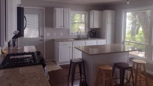 Una cocina con armarios blancos, encimera de granito, estufa y ventana con vistas a árboles.