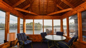 A wooden cabin with a round table and chairs, large windows, and a view of a body of water. - DIRECT ACCESS TO TRAILS 5 and 8, SLEEPS 12, plus PRIVATE LAKE AND TRAILS (Champion)
