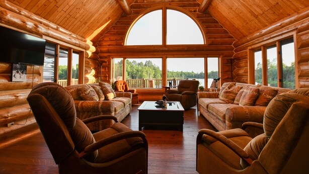 A log cabin interior with a large arched window, wooden walls, and a cozy seating area with sofas and chairs. - DIRECT ACCESS TO TRAILS 5 and 8, SLEEPS 12, plus PRIVATE LAKE AND TRAILS (Champion)