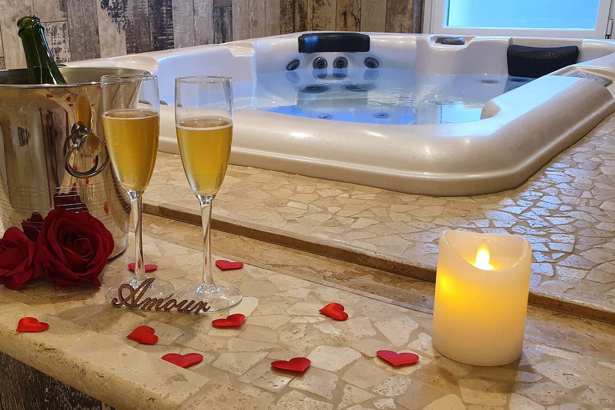 Zona de spa con hidromasaje, copas de champán, rosas y una vela.