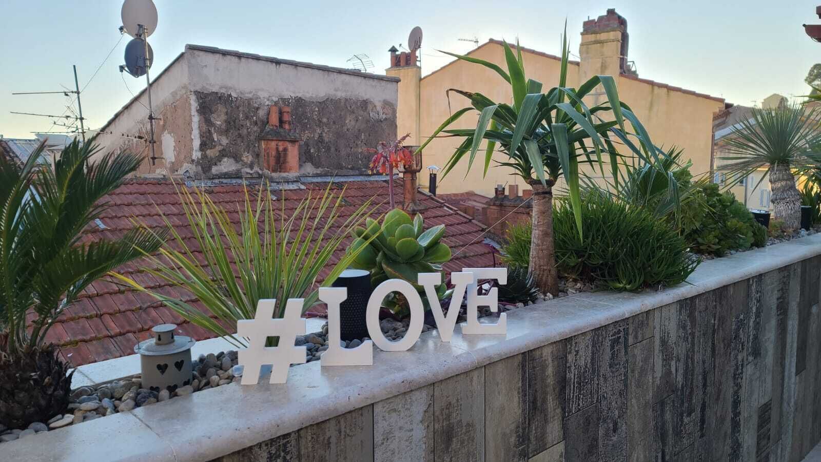 Eine Dachgarten mit einem #LOVE-Schild, Pflanzen und Blick auf Gebäude im Hintergrund.