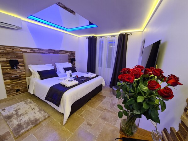 A modern hotel room with a neatly made bed, a vase of red roses, and a flat-screen TV.