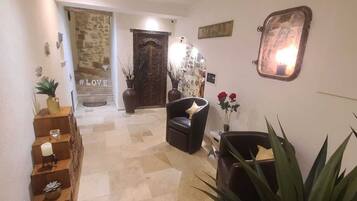 A hallway with a stone wall, a wooden staircase, a black leather chair, and a potted plant.