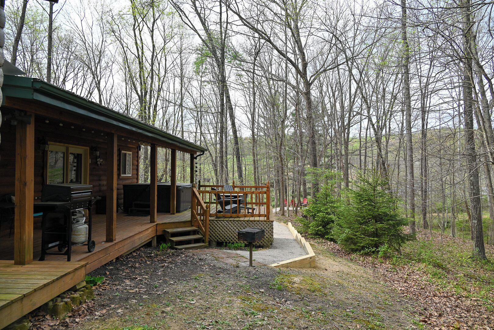 A cabin with a deck, outdoor grill, and hot tub.