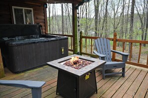 A wooden deck with a hot tub, a fire pit, and a chair. - Beary Cozy Luxury Couples Retreat in Hocking Hills (Laurelville)