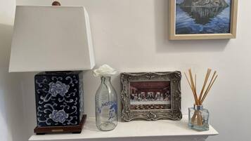 A table with a lamp, a framed picture, a bottle, and reed diffusers.