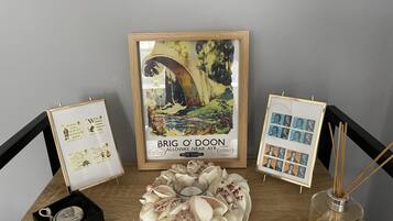 Una obra enmarcada de Brig O'Doon, un póster de ferrocarril de época, rodeada de conchas decorativas y un pequeño candelabro.