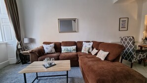A living room with a brown sofa set, a wooden coffee table, and a patterned armchair. - Rose Apartment 2-bed Apt Town Centre Ayr (Ayr)