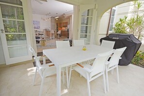 Une table à manger blanche avec des chaises, un barbecue et une vue sur l’intérieur de la maison.