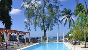 Una piscina con lettini e ombrelloni, circondata da palme e un cielo sereno.