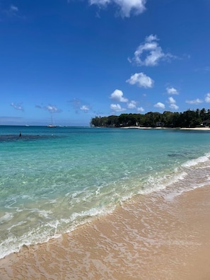 Une plage bordée d’une eau turquoise et limpide, avec de douces vagues et un voilier qui se profile à l’horizon.