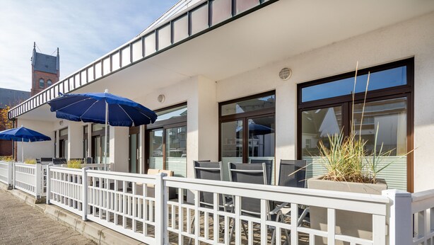 A building with outdoor seating, white railings, and blue umbrellas. - Apartment 1 city center, central, close to the beach and quiet (Norderney)