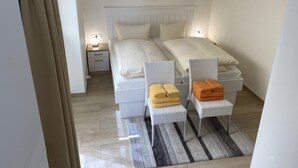 A bedroom with a bed, two bedside tables, a nightstand, a chair, and a rug. - Apartment 1 city center, central, close to the beach and quiet (Norderney)