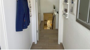 A hallway with a wooden hanger and a blue towel, a door leading to a room with a bed, and a small shelf with items. - Apartment 1 city center, central, close to the beach and quiet (Norderney)