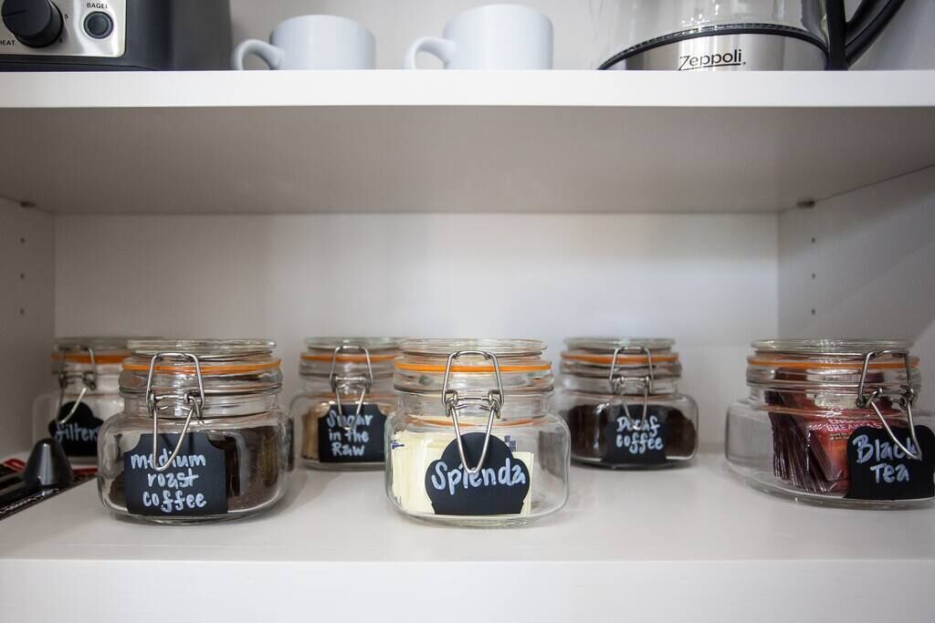 A shelf with several glass jars containing different types of coffee and tea, each labeled with the product name.