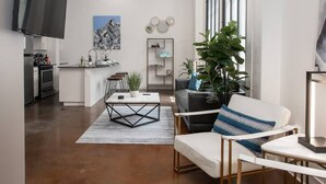A modern living room with a sofa, coffee table, and a TV. There is a kitchen area with a dining table and chairs. - Downtown Fort Worth Luxury Loft in Sundance Square (Fort Worth)