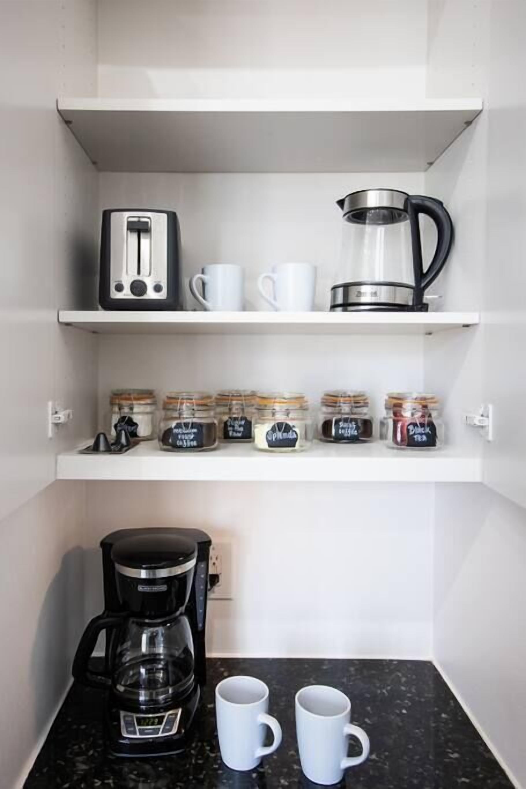 Een keuken met een koffiezetapparaat, twee mokken, een broodrooster, een waterkoker en theepotjes op de planken.