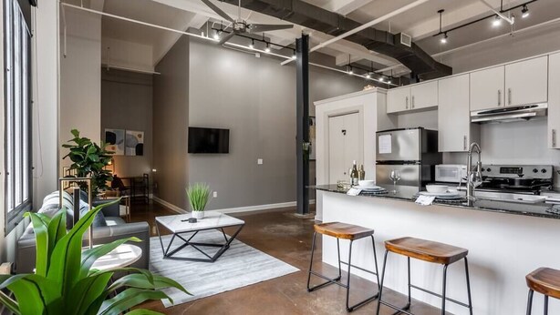 A modern kitchen with white cabinets, stainless steel appliances, and a bar area with stools. - Downtown Fort Worth Luxury Loft in Sundance Square (Fort Worth)