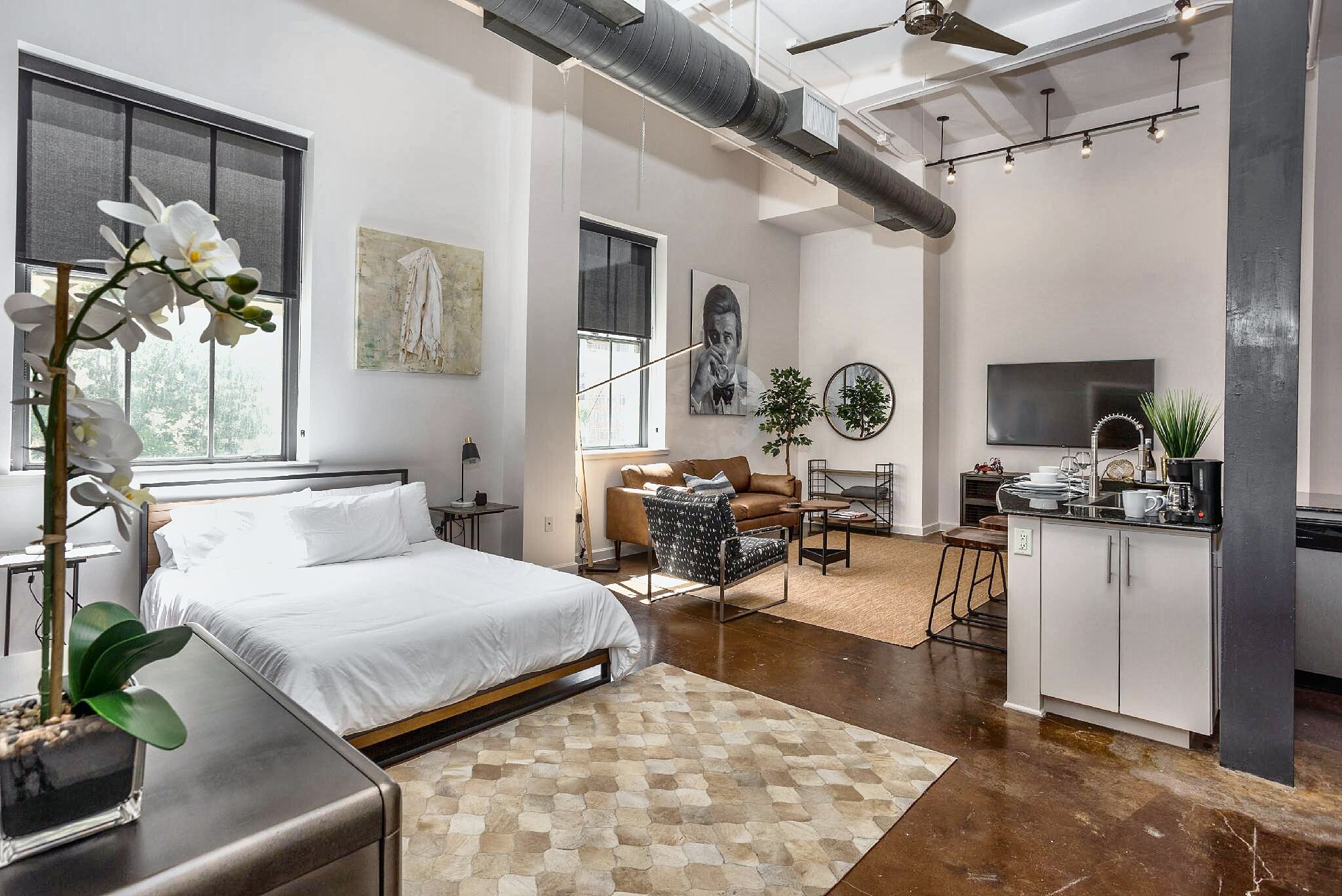 A modern bedroom with a large bed, a desk, and a kitchenette area.