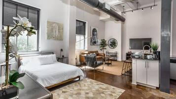 A modern bedroom with a large bed, a desk, and a kitchenette area.