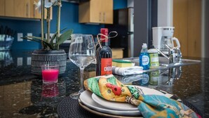 En køkkenbordplade med en orkidé i potte, en Crush-vinflaske, et glas, en kaffemaskine og diverse køkkenredskaber.