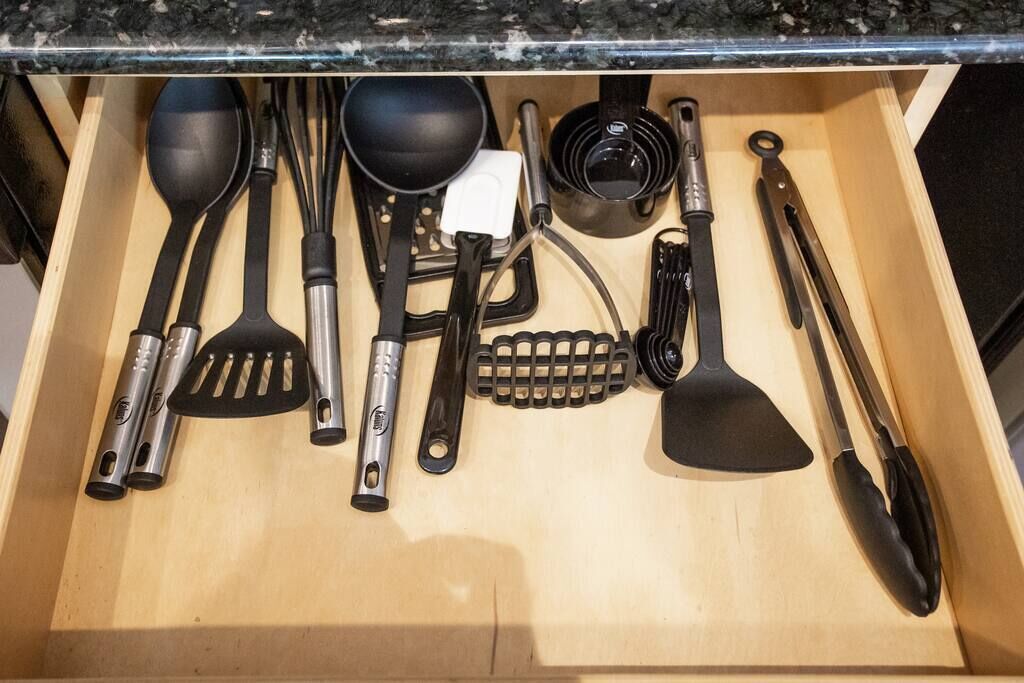 Un cassetto pieno di utensili da cucina assortiti, tra cui spatole, pinze e una grattugia.