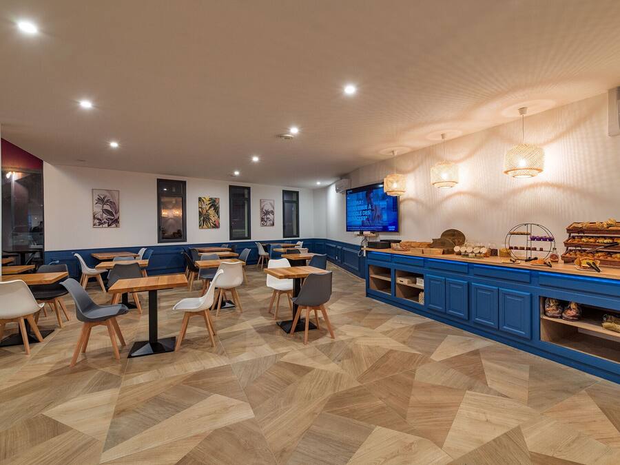 Un café moderno con mesas y sillas de madera, una barra azul con exhibición de alimentos y obras de arte en las paredes.