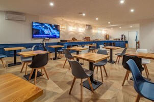 Un comedor moderno con mesas y sillas de madera, una encimera de cocina y un televisor montado en la pared.