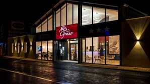 A hotel with a prominent red sign, large windows, and outdoor seating visible through the entrance. - Hôtel Le Cyrano (Bergerac)