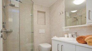 A modern bathroom with a glass-enclosed shower, a toilet, and a vanity with a mirror. - Apartment 2 City center, central, close to the beach and quiet (Norderney)
