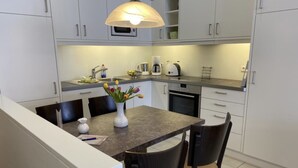 A modern kitchen with white cabinets, a granite countertop, a built-in oven, and a dining area with two chairs and a vase of flowers. - Apartment 2 City center, central, close to the beach and quiet (Norderney)