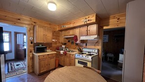 Une cuisine aménagée dans le style d’un chalet en bois, avec une table ronde en bois, un fourneau, un four à micro-ondes et des placards en bois.