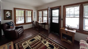 Un salon avec un canapé en cuir marron, une table à manger avec des chaises, un tapis à motifs animaliers et de grandes fenêtres avec des cadres en bois.