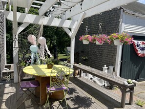 A covered patio with a table and chairs, a hanging light fixture, and a white fence.