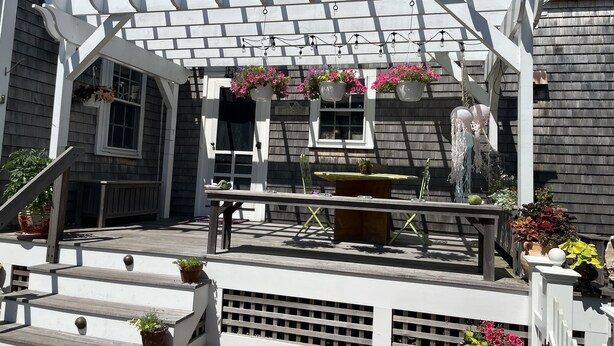 Una casa de dos pisos con un porche, una mesita y cestas de flores colgantes.