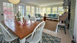 Una habitación amplia con una mesa de comedor de madera, sillas blancas, un sofá y una jaula de pájaros.