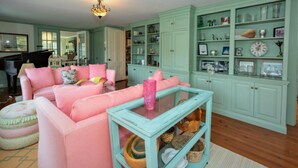 Una sala de estar con un sofá rosa, armarios color aguamarina y una mesa de centro de vidrio.