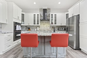 A modern kitchen with white cabinets, a central island with red bar stools, stainless steel appliances, and a tiled backsplash.
