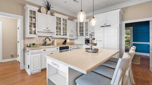 A spacious kitchen with white cabinetry, a central island with seating, and pendant lighting. - Relaxing Waterfront w/ Dock, Easy Drive, On the Lake (Eatonton)