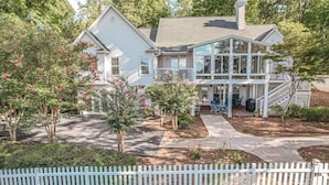 A two-story house with a covered porch, a front yard with trees and shrubs, and a white picket fence. - Relaxing Waterfront w/ Dock, Easy Drive, On the Lake (Eatonton)