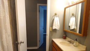 Un baño con tocador de madera, un espejo y una puerta que da a otra habitación.