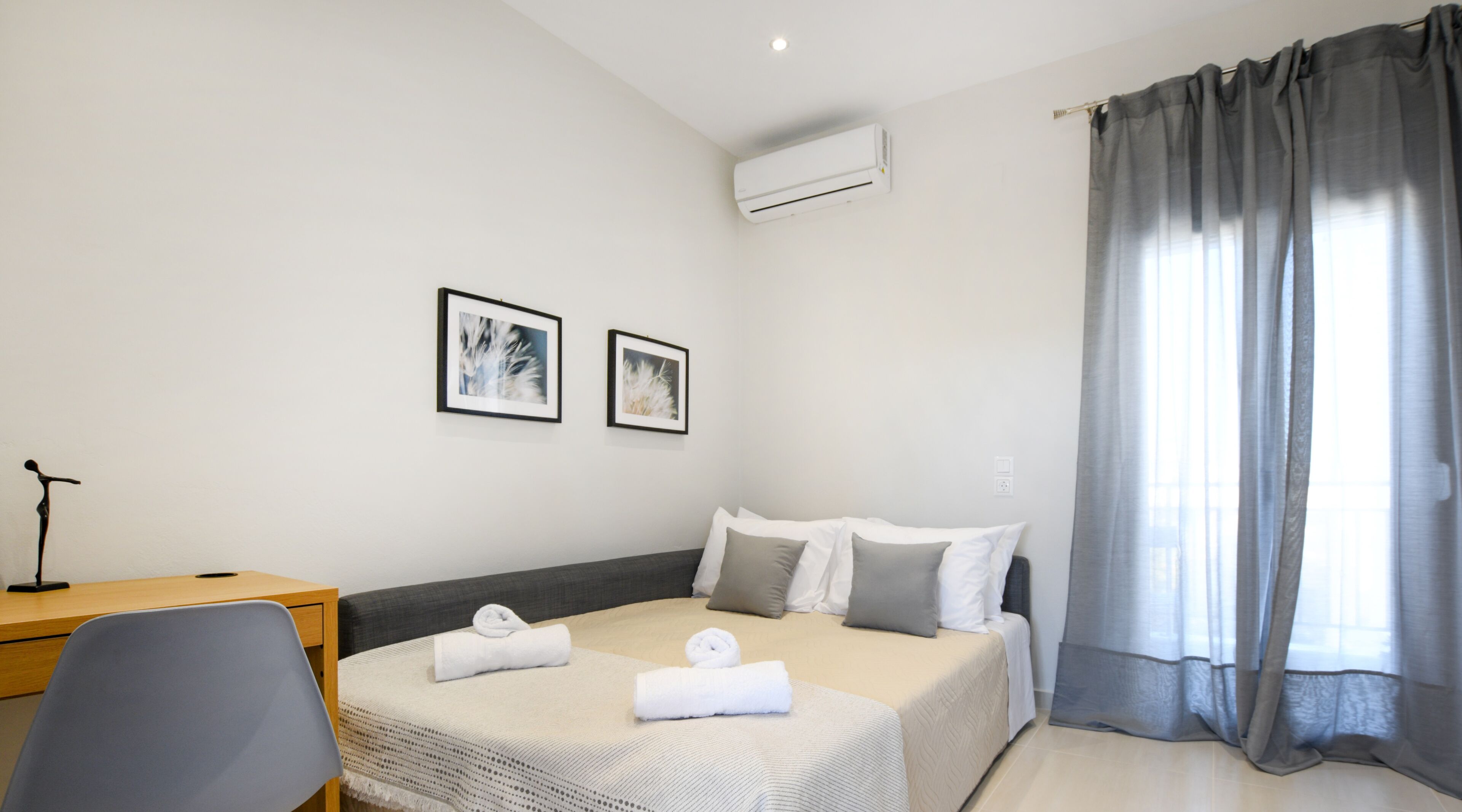 A hotel room with a bed, a desk, two framed pictures, and a window with curtains.
