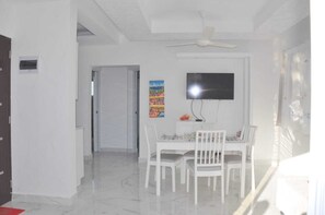 A dining area with a white table and chairs, a ceiling fan, a TV, and a colorful painting on the wall.