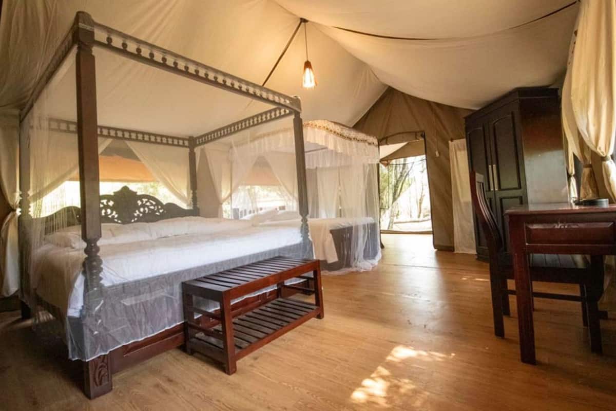 A four-poster bed with a canopy, a wooden bench, a desk, and a chair in a tented room.