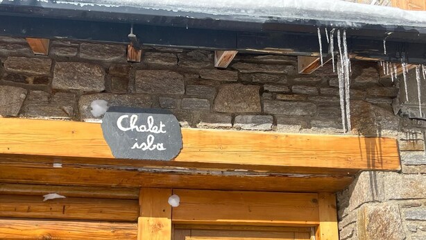 A wooden cabin with a stone wall and a sign that reads "Chalet isba".