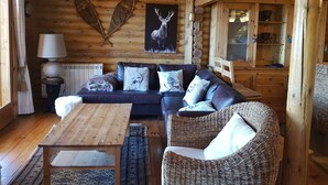 A cozy log cabin interior with a wooden sofa, wicker chair, and a dining table.