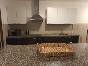A kitchen with dark cabinets, a microwave, a kettle, and a woven basket on the countertop. - Apart Perú Económico 3 (Miraflores)