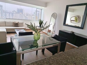 A modern living room with a glass coffee table, a sofa, and a city view. - Apart Perú Económico 3 (Miraflores)